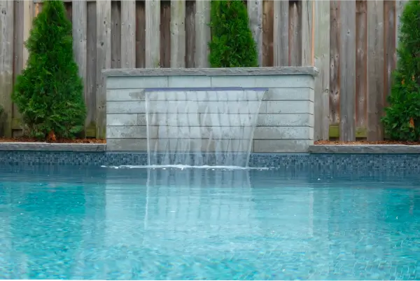 Backyard pool and landscape installation by Boulder Design Pools & Landscapes with pool barrier safety fence, turf grass and waterfall feature